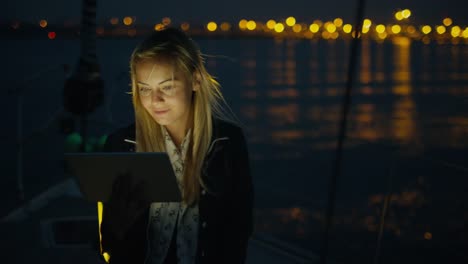 La-chica-está-usando-una-tableta-en-un-velero-en-el-mar-por-la-noche.