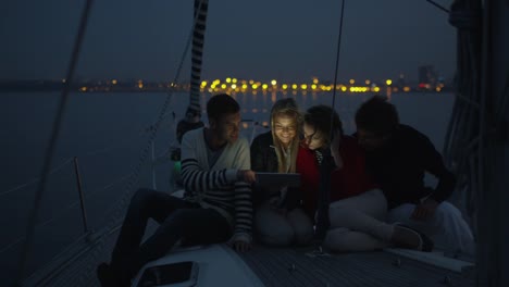 Gruppe-von-Menschen-nutzen-Tablet-auf-einer-Yacht-im-Meer-in-der-Nacht.