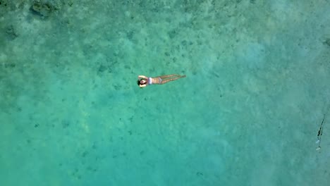 Aerial-view-of-an-attractive-woman-in-a-bikini-floating-in-crystal-clear-sea.-Pretty-beatiful-girl-swimming-in-Indian-ocean