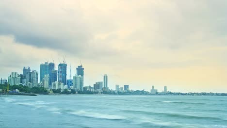 Evening-time-lapse-shot-of-the-clouds-passing-over-the-city-buildings-(city-skyline)-most-of-them-are-under-construction-while-Arabian-sea-in-the-foreground,-Mumbai,-India