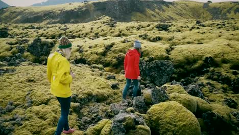 Vista-aérea-de-las-dos-mujeres-caminando-en-el-campo-de-lava-en-Islandia.-Los-turistas-toca-las-protuberancias-de-musgo