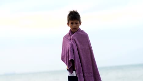 tired-sad-refugee-boy-in-a-towel-stands-alone-looking-into-the-camera,-boy-is-trying-to-keep-warm