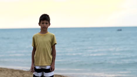 boy-stands-on-the-beach-near-the-sea-and-looks-at-the-camera
