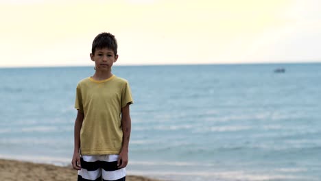 niño-se-encuentra-en-la-playa-cerca-del-mar-y-mira-a-la-cámara