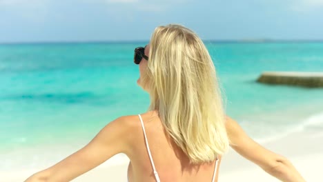 Retrato-de-la-hermosa-mujer-rubia-con-gafas-de-sol-posando-y-sonriendo-en-la-playa,-levantar-los-brazos.-En-la-localidad-de-mar-de-fondo.