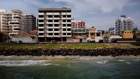 Drone-flying-right-along-ocean-coast-street-in-Colombo-Sri-Lanka.-Aerial-tracking-shot-of-traffic-vehicles-and-buildings