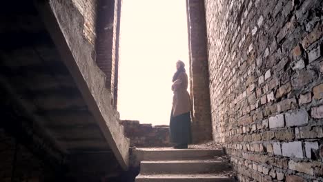 Young-refugee-muslim-woman-in-hijab-standing-alone-in-abandoned-building-and-looking-around,-worried-and-terrified