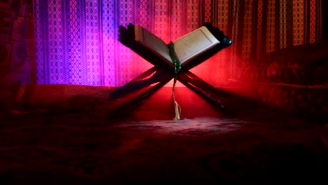 Open-holy-book-of-Muslims-on-stand-on-eastern-carpet-with-dark-toned-foggy-background.-Muslim-religion-concept.-Selective-focus.-Slider-shot.