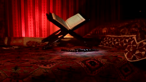 Open-holy-book-of-Muslims-on-stand-on-eastern-carpet-with-dark-toned-foggy-background.-Muslim-religion-concept.-Selective-focus.-Slider-shot.