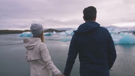 Young-couple-looking-at-Jokulsarlon-glacier-lake-in-Iceland,-cinematic-shot