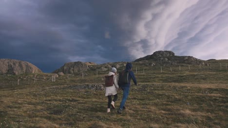 Young-loving-couple-running-in-field-on-background-of-epic-dramatic-clouds,-slow-motion