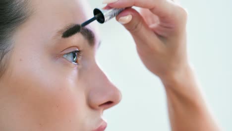 Female-hand-combing-brow-young-beautiful-woman-using-brush-or-mascara-closeup