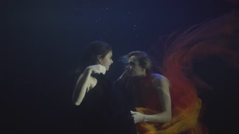 Two-sexy-woman-in-chiffon-dress-swimming-together-underwater-in-dark-pool