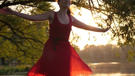 Woman-in-red-transparent-dress-dancing-and-spinning-around-against-lake-at-sunset