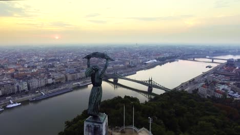 Flying-around-of-Statue-of-Liberty-with-the-skyline-of-Budapest-at-background.-Budapest,-Hungary---4K-aerial-footage-at-sunrise