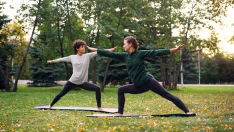 Erfahrener-Instruktor-schlanke-Mädchen-lehrt-ihre-Studentin-Hatha-Yoga-Asanas-auf-warmen-Herbsttag-im-Stadtpark.-Gesunde-Lebensweise-und-Sport-für-urbane-Menschen-Konzept.