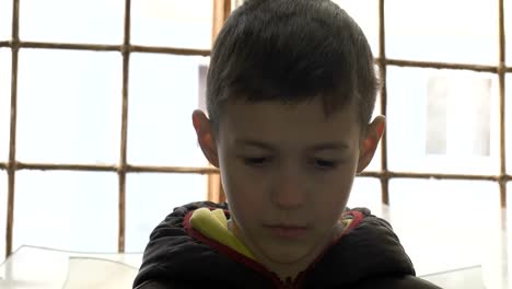 portrait-emaciated-refugee-boy-stands-alone-near-a-broken-window,-looking-into-the-camera