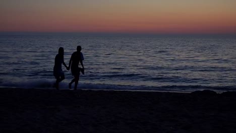 Pareja-de-enamorados-caminando-por-la-orilla-del-mar-al-atardecer,-romántico-paseo