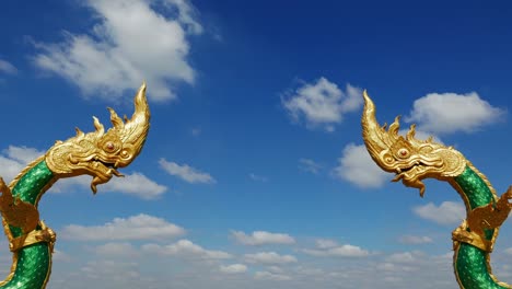 Dragon-statues-facing-each-other-at-Nakhon-Phanom,-Thailand.-Naga,-symbol-of-protection.-Time-lapse,-moving-clouds-against-clear-blue-sky.