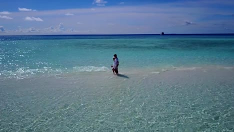 v03909-Aerial-flying-drone-view-of-Maldives-white-sandy-beach-2-people-young-couple-man-woman-romantic-love-on-sunny-tropical-paradise-island-with-aqua-blue-sky-sea-water-ocean-4k