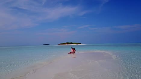 v03877-Aerial-flying-drone-view-of-Maldives-white-sandy-beach-2-people-young-couple-man-woman-romantic-love-on-sunny-tropical-paradise-island-with-aqua-blue-sky-sea-water-ocean-4k