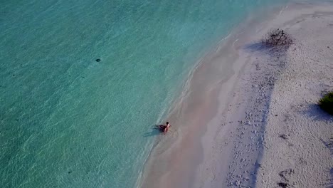 v03951-Aerial-flying-drone-view-of-Maldives-white-sandy-beach-2-people-young-couple-man-woman-romantic-love-on-sunny-tropical-paradise-island-with-aqua-blue-sky-sea-water-ocean-4k