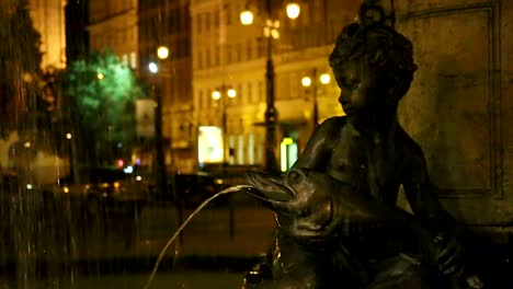 Statue-of-boy-sitting-on-fountain-holding-fish-at-night,-romanticism