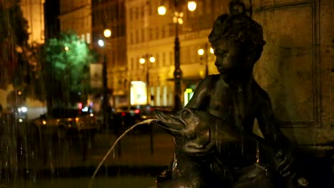 Statue-of-boy-sitting-on-fountain-holding-fish-at-night,-pan,-romanticism