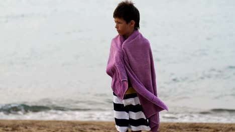 tired-sad-refugee-boy-in-a-towel-stands-alone-looking-into-the-camera,-boy-is-trying-to-keep-warm