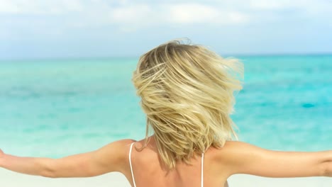 Portrait-of-the-Beautiful-Blonde-Woman-Wearing-Sunglasses-Posing-and-Smiling-on-the-Beach.-In-the-Background-Sea-Resort.