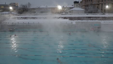 Dampf-steigt-langsam-über-ein-offenes-Schwimmbad-im-winter