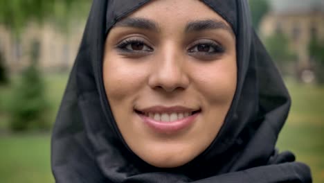 Face-of-young-sencere-muslim-girl-in-hijab-is-smiling-in-daytime,-in-bad-weather,-watching-at-camera,-religiuos-concept,-blurred-background