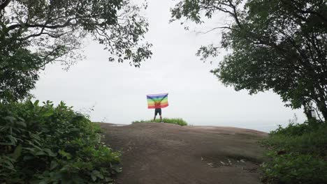 hombre-levantar-bandera-LGBTI-de-color-arco-iris-ondeando-en-duro-viento-en-el-mirador-de-alta-montaña