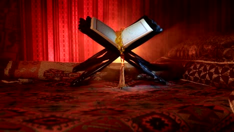 Open-holy-book-of-Muslims-on-stand-on-eastern-carpet-with-dark-toned-foggy-background.-Muslim-religion-concept.-Selective-focus.-Slider-shot.