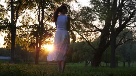 Frau-in-weißem-Kleid-Sonnenuntergang-genießen-im-Park,-Ansicht-Rückseite