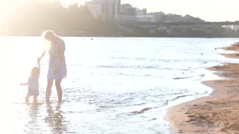 Mom-and-girl-playing-on-the-beach-of-the-river-at-sunset-and-swim.