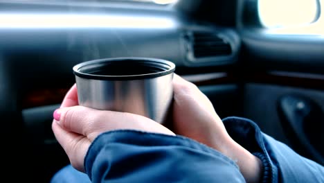 Closeup-view-of-woman's-hands-keeping-a-cup-of-hot-tea-from-thermos-sitting-in-the-car-in-winter.