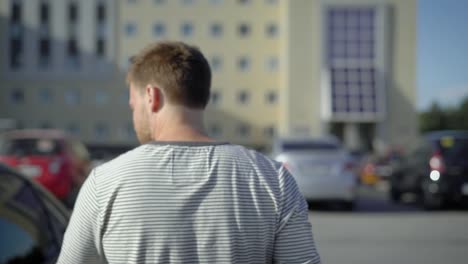 adult-handsome-man-is-walking-over-outdoors-parking-area-in-sunny-summer-day,-opening-doors-of-his-car-and-sitting-inside