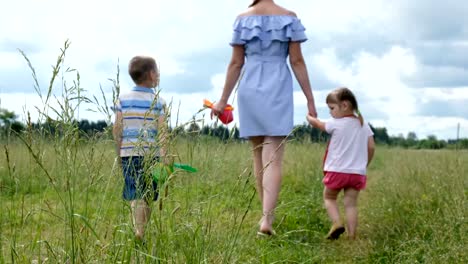 Young-mother-with-two-young-children-walking-in-the-field-on-the-grass-in-summer.-Happy-family-on-a-walk.