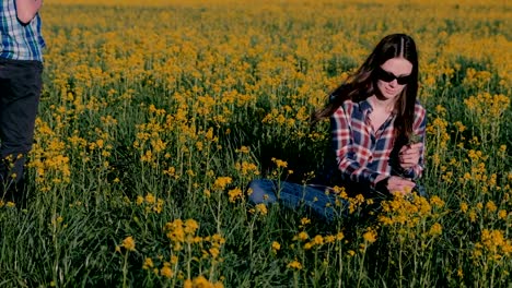 Junge-gibt-seiner-Mutter-ein-Bouquet-von-wilden-Blumen-und-küsst-sie-sitzen-auf-dem-Rasen-unter-den-gelben-Blumen.