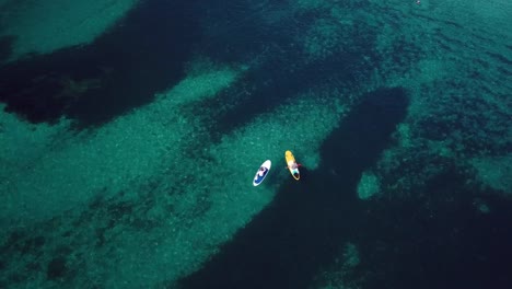 Video-from-above,-aerial-view-of--two-people-on-a-stand-up-paddle-(SUP)-in-Sardinia,-Italy.