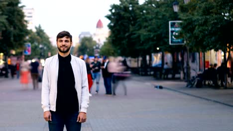 Time-lapse-of-good-looking-bearded-guy-looking-at-camera-and-smiling-standing-in-the-street-downtown-then-stepping-back-while-men-and-women-are-moving-near-him.