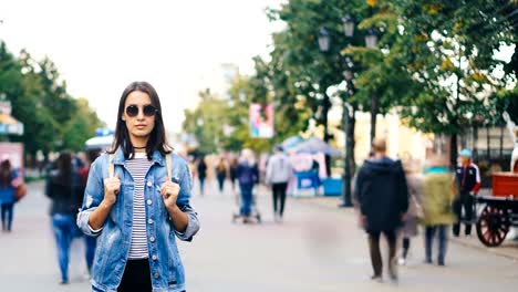 Time-lapse-of-lonely-girl-tourist-standing-in-modern-city-with-people-moving-around-and-looking-at-camera.-Youth-lifestyle,-society-and-loneliness-concept.