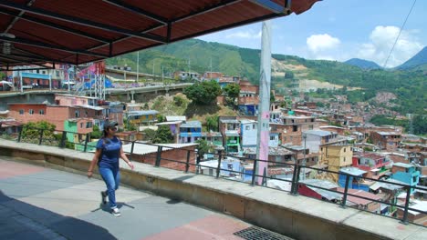 Girl-walks-on-walkway-under-roof-with-view-of-Comuna-13-neighborhood,-Medellin-Colombia