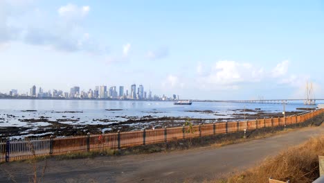 Cyclists-and-people-on-narrow-sidewalk-near-Mumbai-Worli-sea-link-skyline.