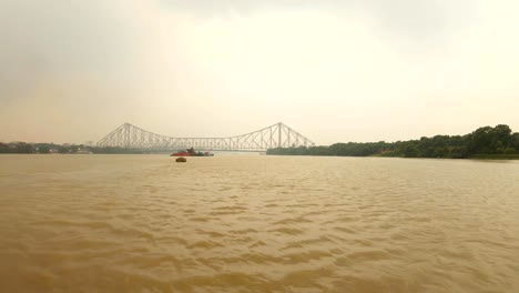 Howrah-Brücke-voll-fließender-Fluss-Hoogli-Barge-schwimmt-Gebäude-und-Bäume-an-Ufern-bewölkten-Tag