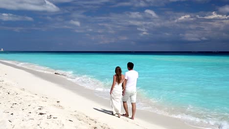 Young-beautiful-newlyweds-in-love-holding-hands-and-walking-on-tropical--beach