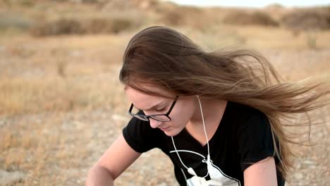 Teenager-Mädchen-mit-eyeglasses-sitzt-auf-dem-Boden,-hören-die-Musik-im-Freien