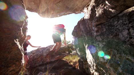 Hiking-Couple-holding-hands-to-climb-rock-in-nature