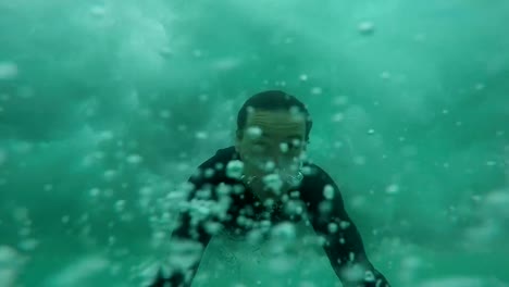 SLOW-MOTION-CLOSE-UP:-Cheerful-young-surfer-duck-diving-under-the-wave